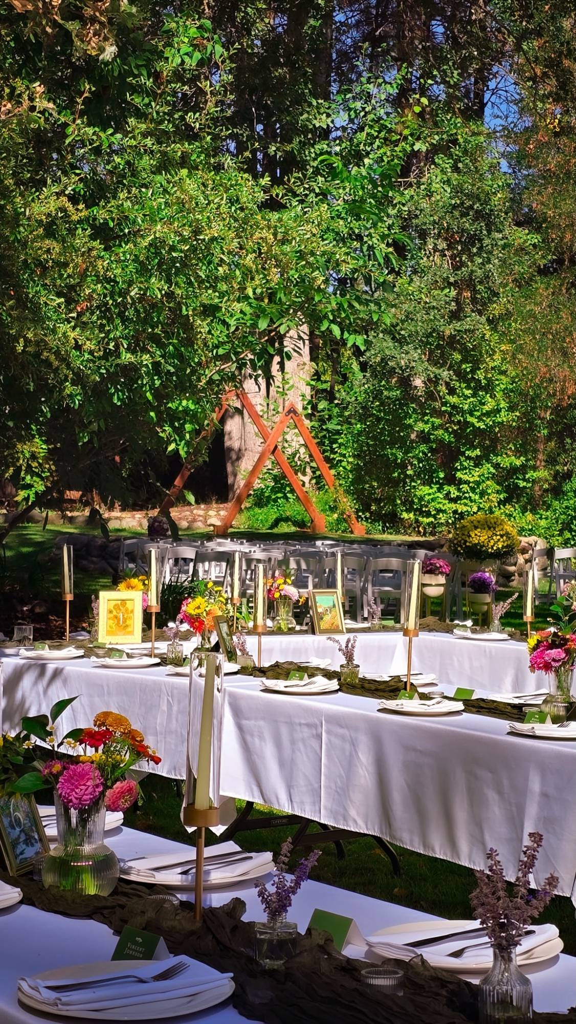 Wedding reception tables set beneath the trees near the ceremony arch